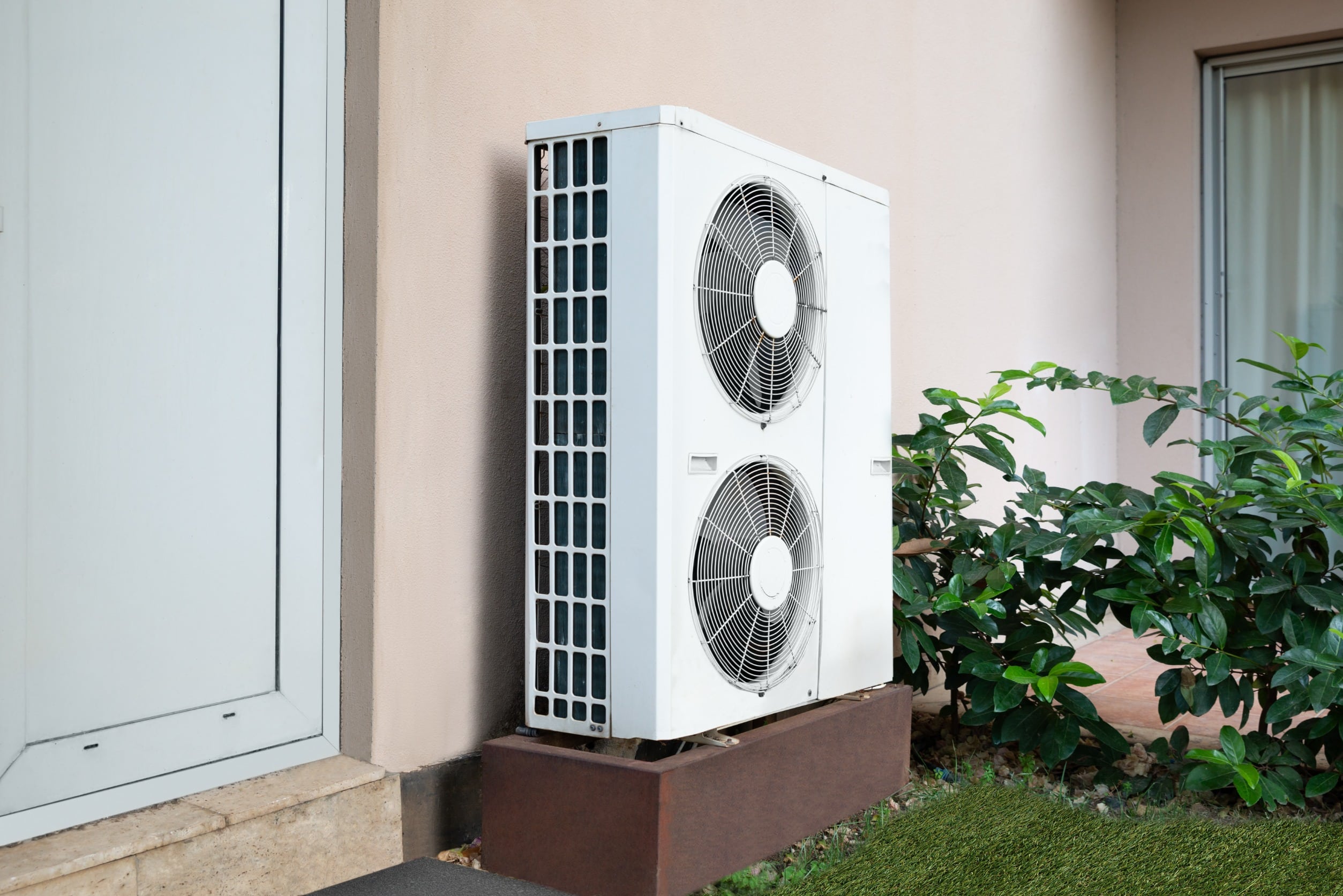 an outdoor air conditioning unit installed on a platform against the wall of a home