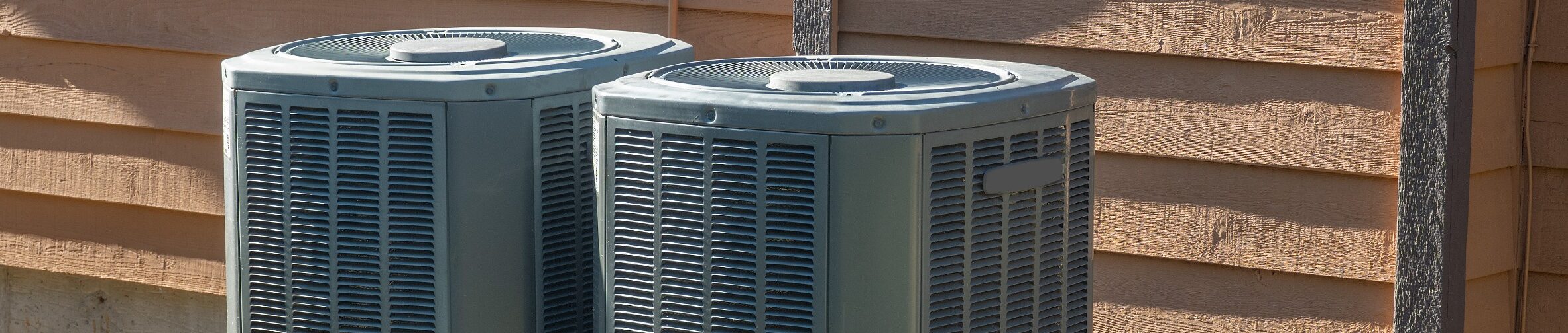 two hvac systems outside of a home next to a patch of yellow flowers