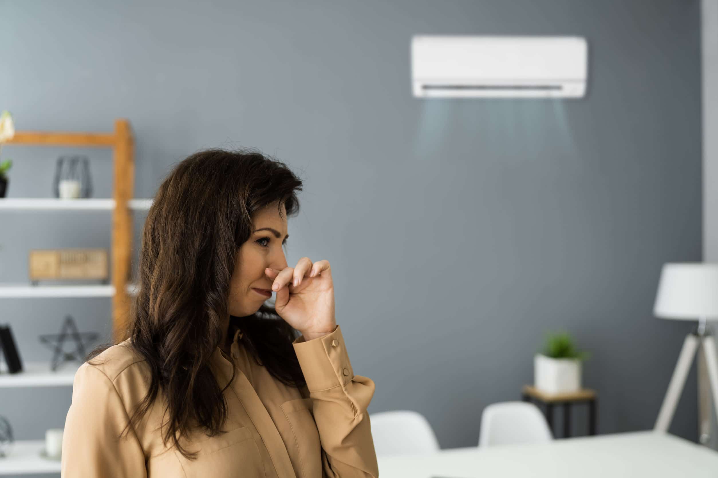 woman covering her nose to block a smell coming from the ductless ac unit behind her