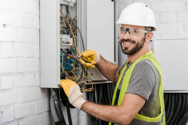 electrician repairing electrical box with pliers in corridor and looking at camera